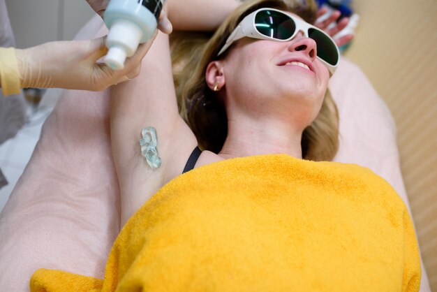 The cosmetologist does the laser hair removal procedure in the armpit zone