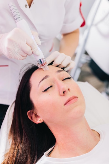 cosmetologist doing hydrafacial treatment on woman face in beauty clinic