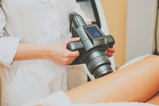 Foto cosmetologo che fa massaggio con l'apparato sulle gambe del cliente femminile, primi piani.