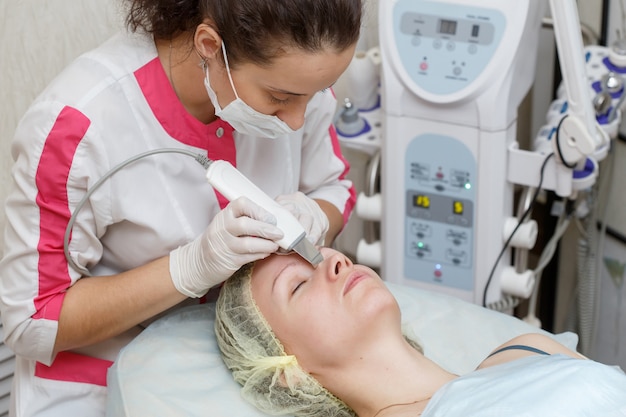 Cosmetologist doing procedure of cleaning the face with ultrasonic scrubber