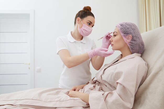 Cosmetologist drawing mark on client face to prepare for rejuvenation treatment