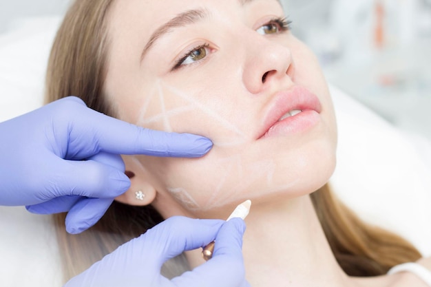 Photo the cosmetologist draws contours with a white pencil on the patient's face schematic marking before drawing contours preparing a closeup face for cosmetic procedures