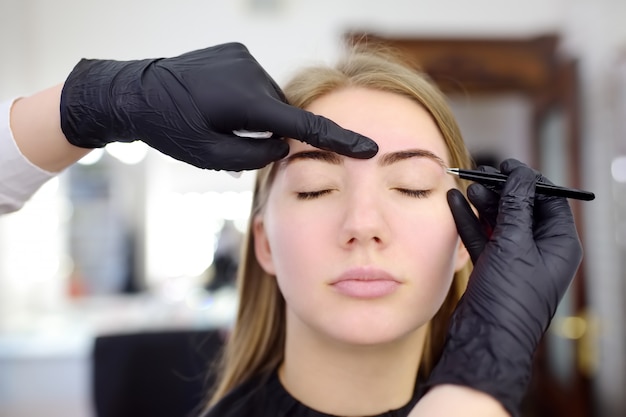 Photo cosmetologist eyebrow plucking. attractive woman getting facial care and makeup at beauty salon. architecture eyebrows.