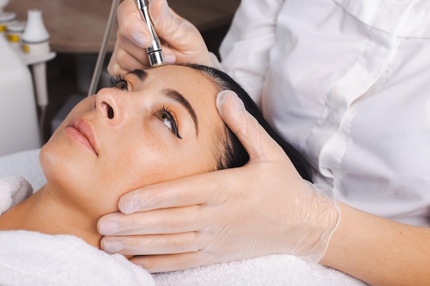 Cosmetologist hands making the procedure microdermabrasion of the facial skin of a client at the spa...