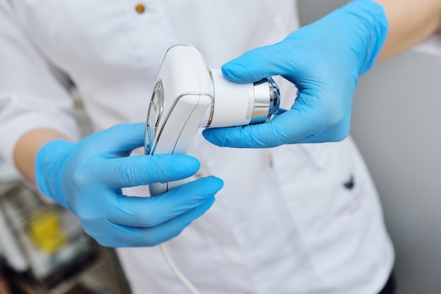 The cosmetologist holds a device for computer diagnostics of the structure and condition of the hair - a trichoscope.