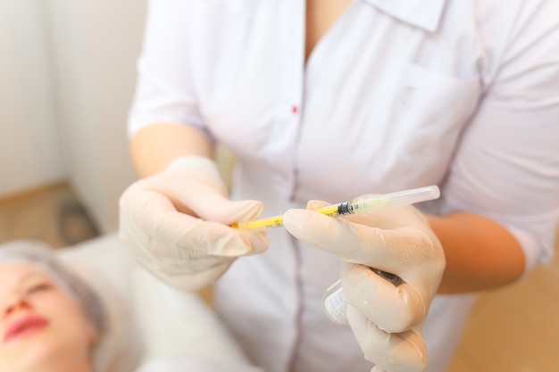 the cosmetologist holds a syringe in front of the client's face while preparing for the botox procedure