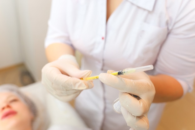 The cosmetologist holds a syringe in front of the client's face while preparing for the botox procedure