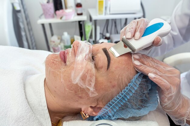 Photo cosmetologist in latex gloves applies a rejuvenating mask to a woman's face with a spatula