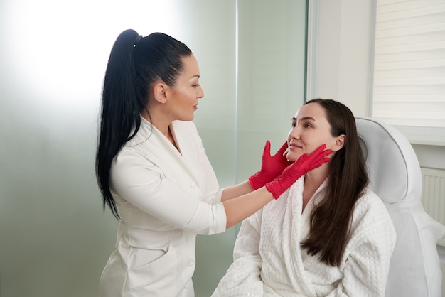 Cosmetologist looking at female face checking skin condition during skin examination in beauty salon