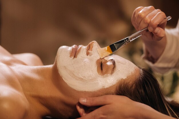 A cosmetologist makes a mask for a woman\'s face to rejuvenate\
the skin cosmetology