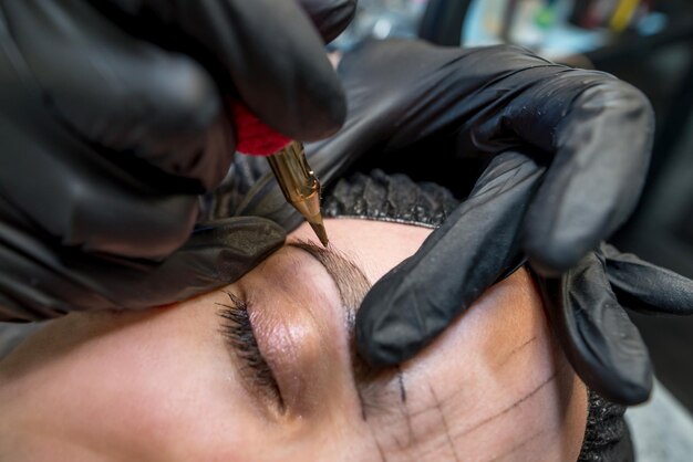 Photo the cosmetologist makes a permanent makeup of the eyebrows on a woman's face