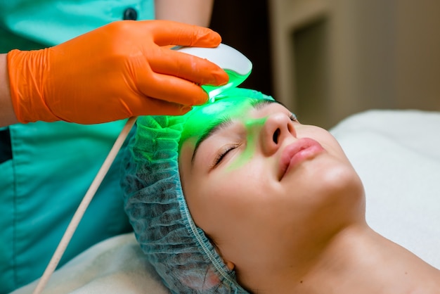 Photo the cosmetologist makes a procedure of hardware face cleaning with a soft rotating brush