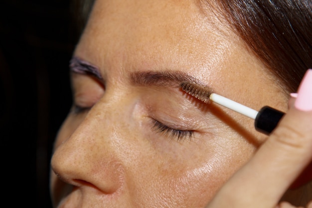 Cosmetologist - makeup artist paints henna on previously plucked, design, trimmed eyebrows in a beauty salon in a correction session. Professional facial.