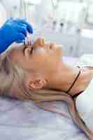 Photo cosmetologist making apparatus phonophoresis facail procedure for woman in beauty salon