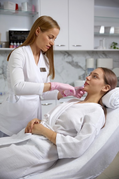Косметолог делает процедуру омолаживающих инъекций лица для подтяжки и разглаживания морщин на женском лице