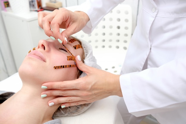 Cosmetologist making taping face procedure using tiger colored tapes in beauty parlor