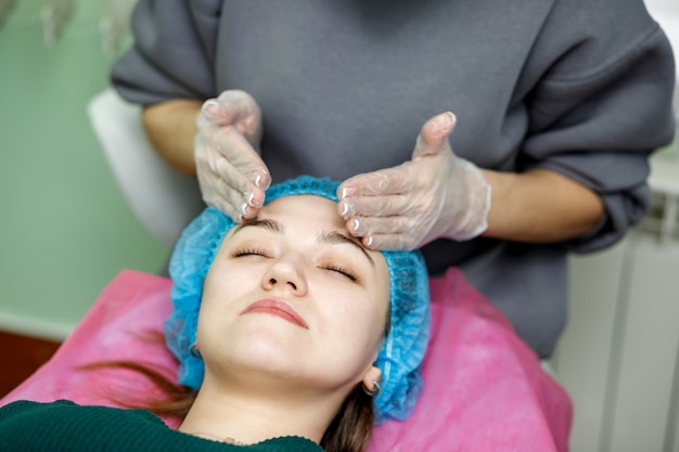 Cosmetologist massages the face of a young girl lying on a couch