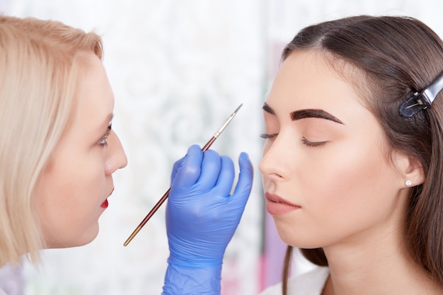 Cosmetologist painting eyebrows with brush for client.