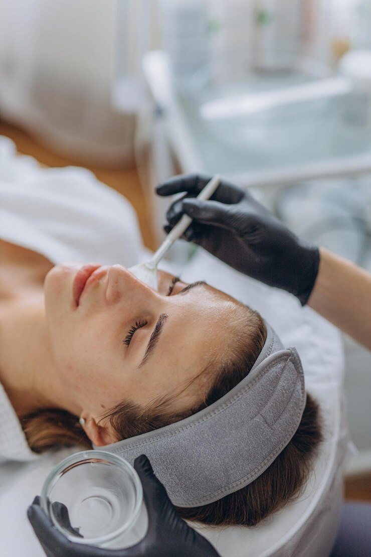 Photo cosmetologist performs a facial peeling procedure on a young woman
