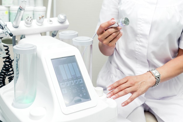 Cosmetologist posing next to a cosmetology machine and an ultrasonic head in his hand. Horizontal photo