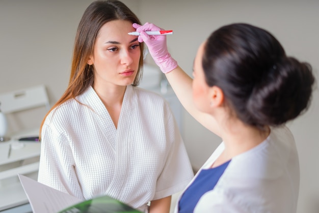 Cosmetologist ready to paint lines with marker on patient face