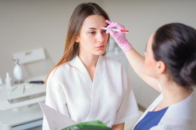 Cosmetologist ready to paint lines with marker on patient face