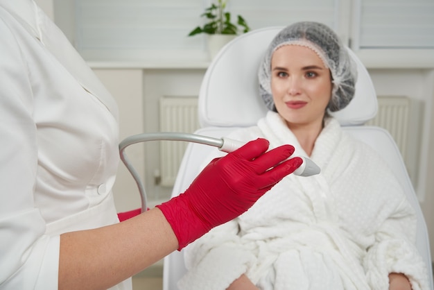 Cosmetologist showing client special medical equipment cosmetologist using modern equipment