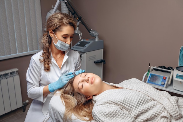 Специалист-косметолог в защитной маске держит в руках шприц с инъекционным составом и готовится к процедуре мезотерапии
