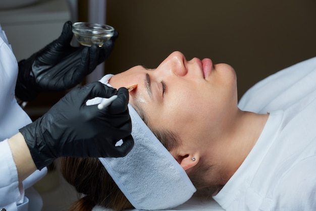 cosmetologist uses brush to apply transparent face peeling to woman.