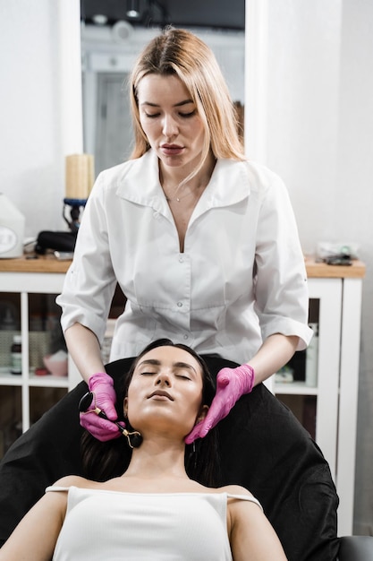 Косметолог использует каменный валик для массажа лица пациентке Массаж лица косметическим валиком в косметологической клинике Процесс массажа лица черным каменным валиком крупным планом