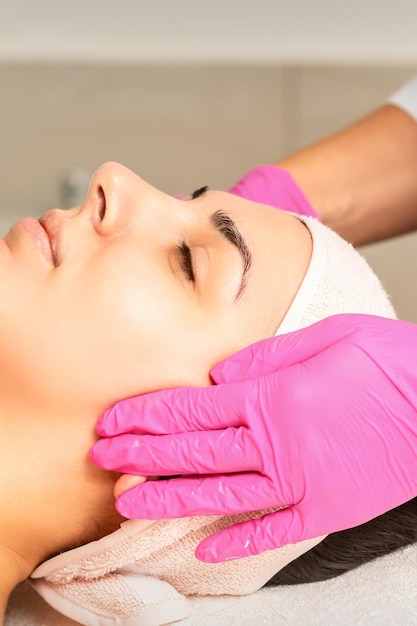 Cosmetologist with gloved hands applies a moisturizing mask with peeling cream on the female face Facial cosmetology treatment Procedures for facial care