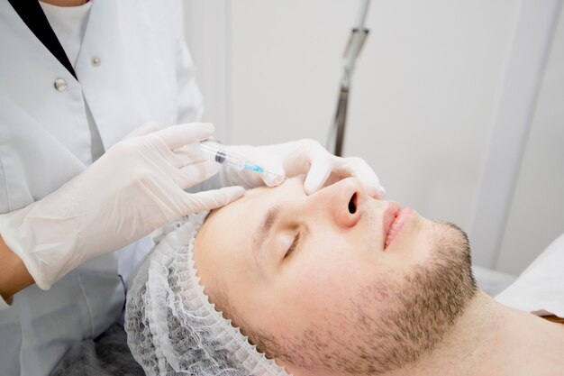 Cosmetologists making injections to mans face to remove scars and wrinkles and make it smooth.