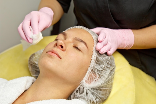 Cosmetology concept Close Beautician hands cleaning and touching a female face with a sponge A woman is lying and resting