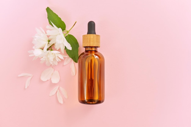 Косметология, лечение, красота, натуральный органический косметический продукт в бутылке с цветами жасмина на розовом фоне, вид сверху