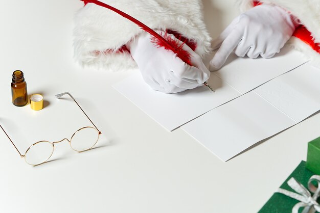 Costumed hands of Santa Claus writing a Christmas letter or greeting on a postcard. close up