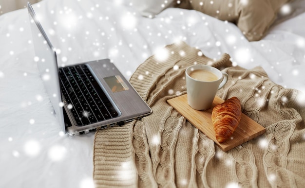 cosy home interior and winter concept cozy bedroom with laptop computer coffee cup and croissant on bed over snow