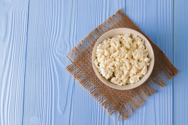 Cottage cheese in bowl on blue wooden board, top view