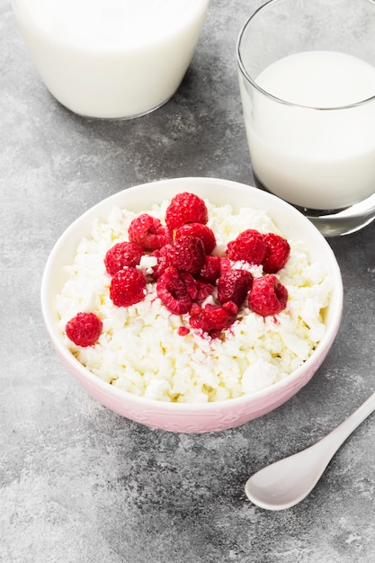 Cottage cheese in bowl with frozen raspberry and milk in glass on a light background