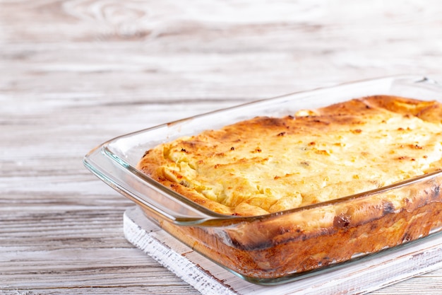 Cottage cheese braadpan met rozijnen in een glazen ovenschaal op een witte houten tafel