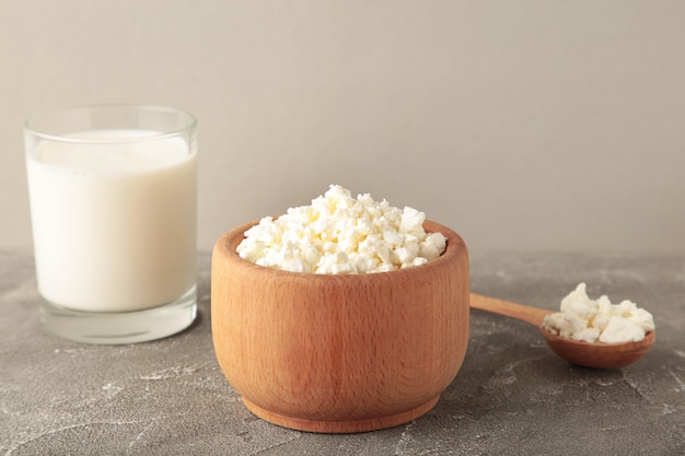 Cottage cheese for breakfast in wooden bowl with milk on grey background.