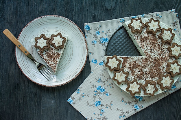 Cottage cheese cake is decorated with cookies and grated black chocolate on dark wood