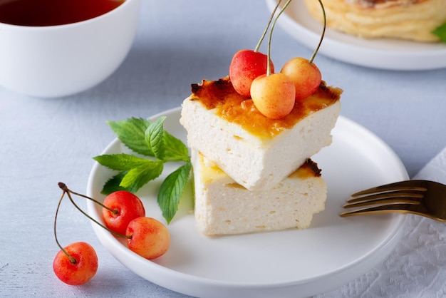 Cottage cheese casserole and sweet cherry on wooden light table Cottage cheese casserole