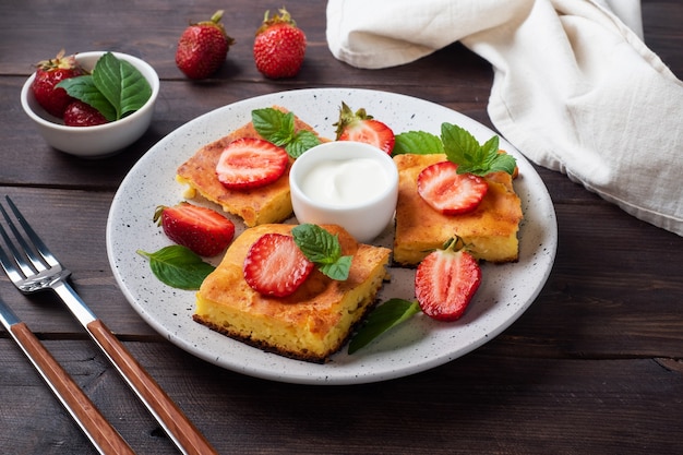 Cottage cheese casserole with strawberries and mint. Delicious homemade dessert made of curd and fresh berries with cream. dark wooden background, copy space.