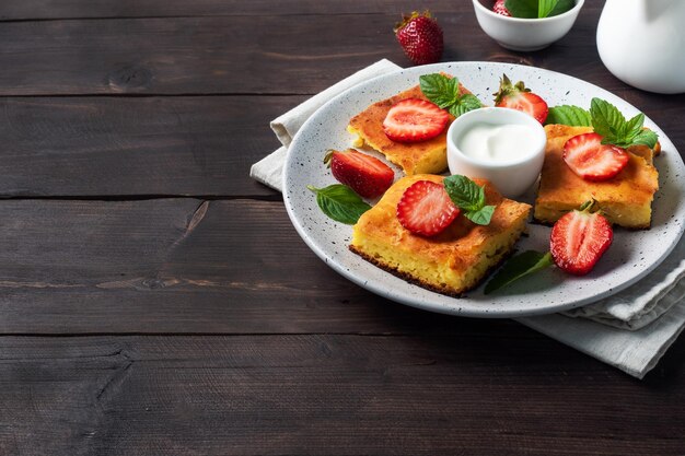 Cottage cheese casserole with strawberries and mint. Delicious homemade dessert made of curd and fresh berries with cream. dark wooden background, copy space.