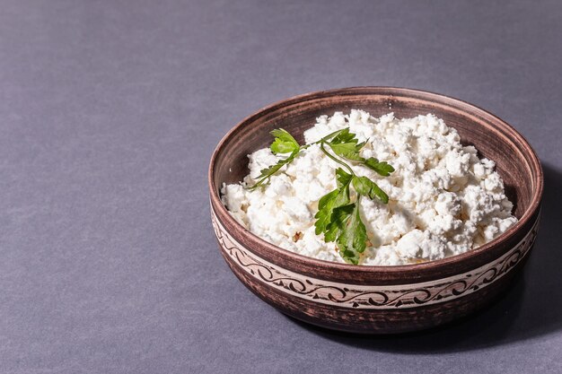 Cottage cheese in a ceramic bowl. Homemade dairy product on a deep plate. Dark grey background, place for text