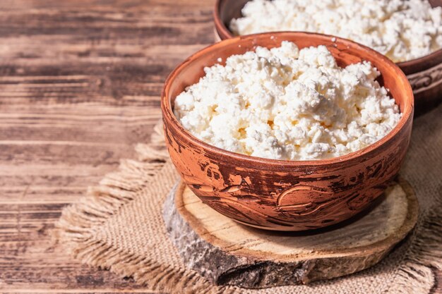 Cottage cheese in a ceramic bowl. Homemade dairy product on a deep plate. Old wooden table, place for text