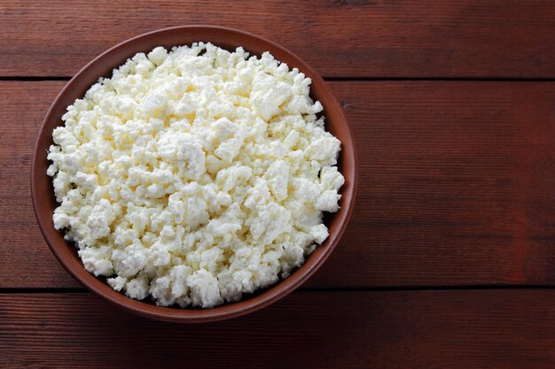 Cottage cheese in clay plate on wooden boards Soft cheese on wooden background Close up