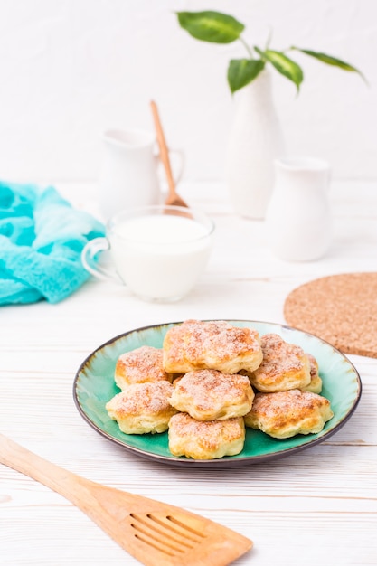 Cottage cheese cookies sprinkled with sugar on a plate and a cup of milk on a wooden table