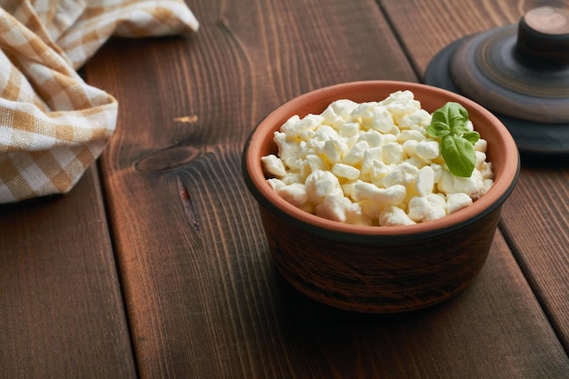 Cottage cheese curd in a brown bowl on wooden background