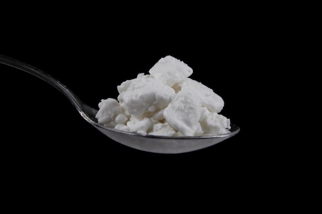 Cottage cheese in metal spoon isolated on black background. Side view of Curdled milk solids